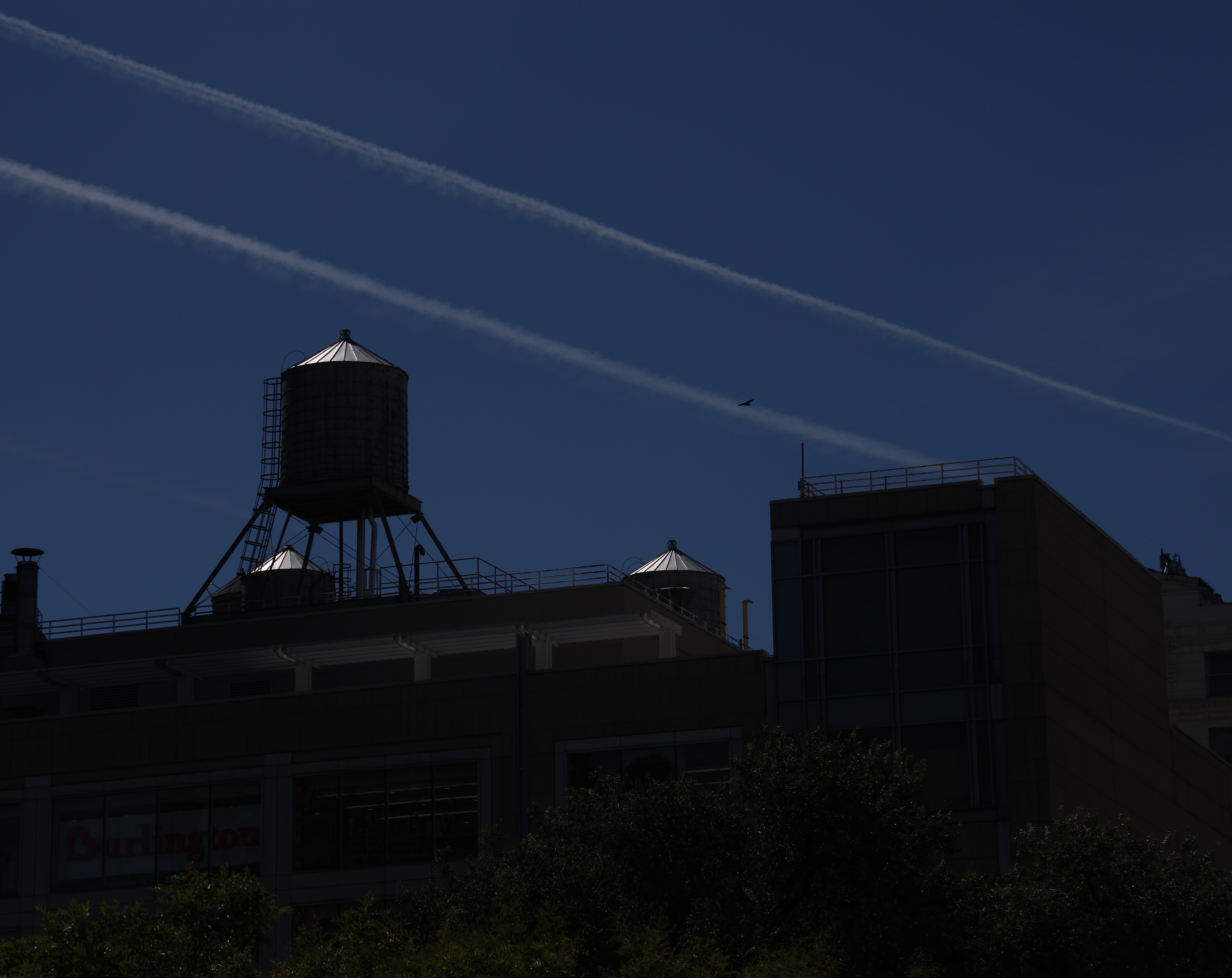 New York rooftop water towers and airplane trails against a dark blue sky