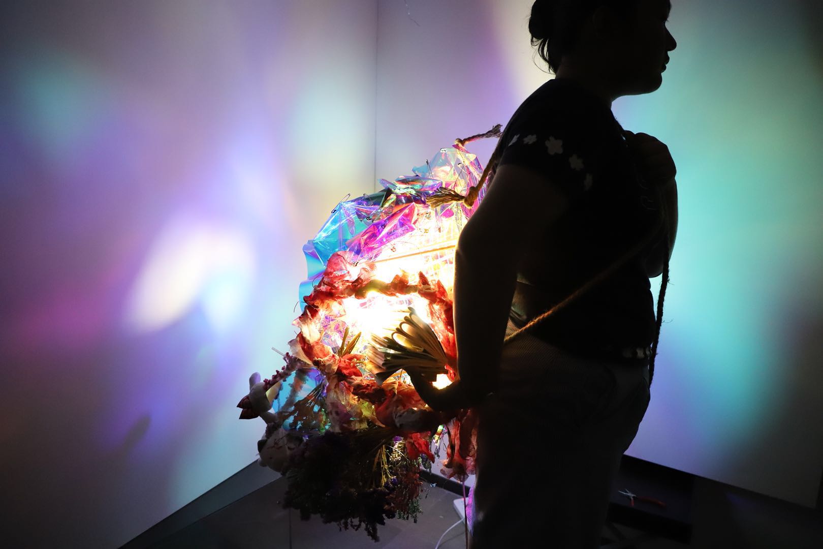 Wearable light sculpture carried on the body, casting colorful light in a dark space
